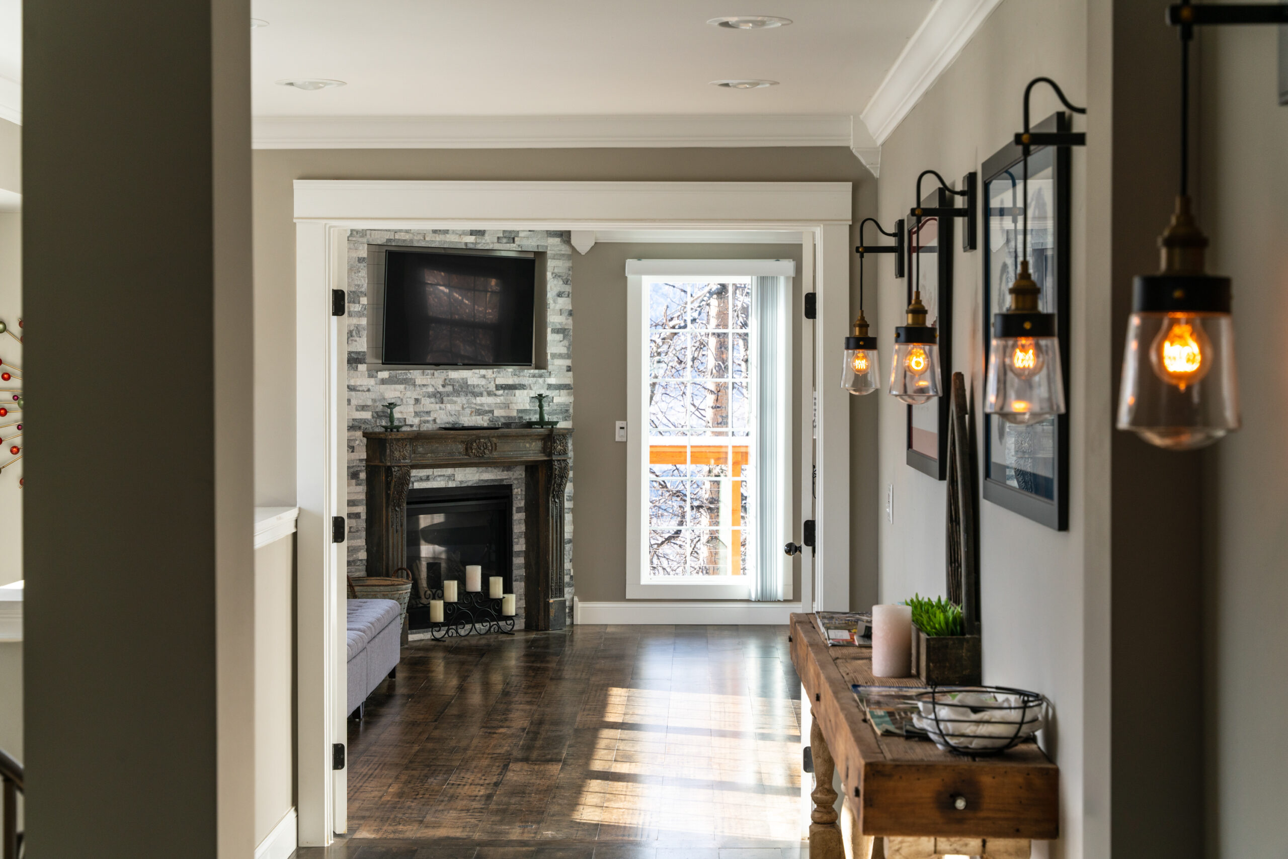 Experience the warmth and elegance of this modern living room, featuring a stone fireplace, chic hanging lights, and a picturesque snowy view, captured by Photos in the House.