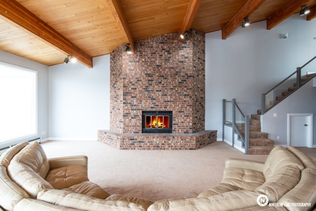 Bright living room in a Seattle home featuring a large brick fireplace with a fire, vaulted wood beam ceilings, and comfortable seating. Ideal for real estate and design inspiration.