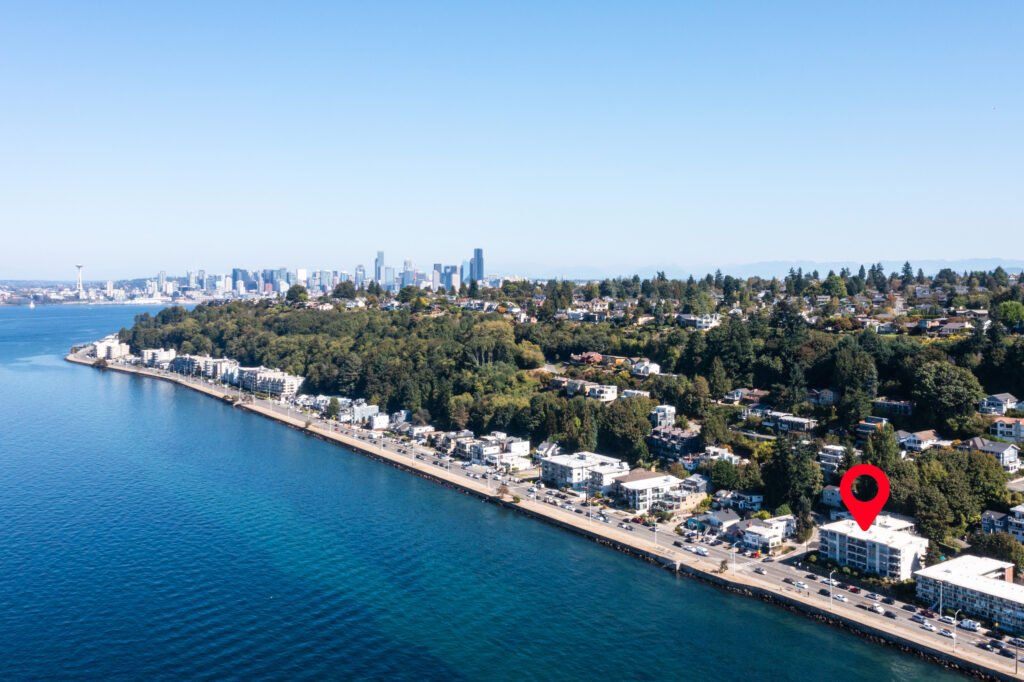 Aerial view of West Seattle waterfront condos on Alki Beach with Seattle downtown skyline and Puget Sound on clear day.