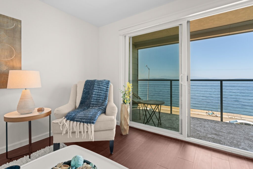 Staged waterfront condo living room with water view through glass doors and modern coastal decor