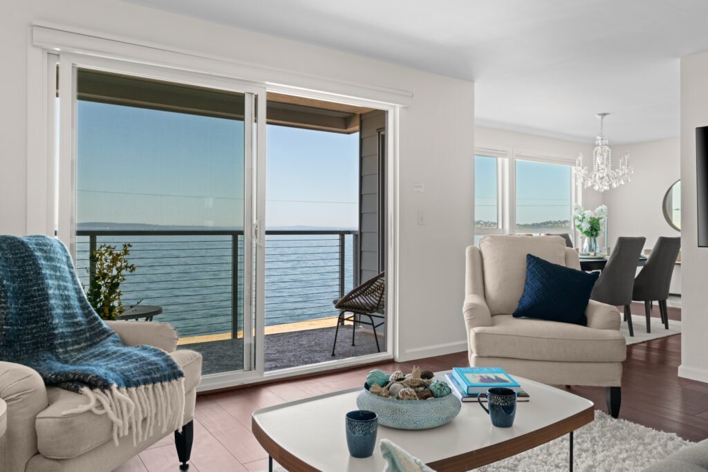 Modern waterfront condo living room with sliding glass doors opening to balcony overlooking Puget Sound.