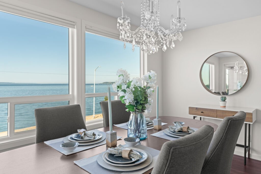 Elegant dining room with crystal chandelier and panoramic Puget Sound and Olympic Mountain views through large windows.