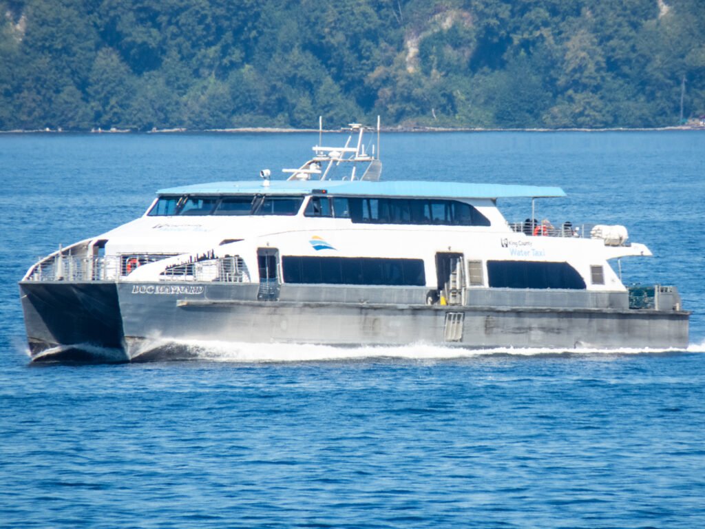 King County Water Taxi catamaran ferry moving across Puget Sound with forested shoreline backdrop.