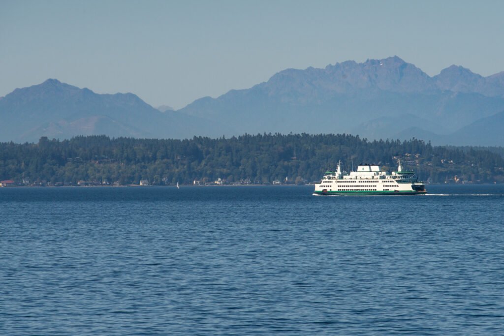 Washington State ferry crossing Puget Sound with Olympic Mountains and forested shoreline in background.