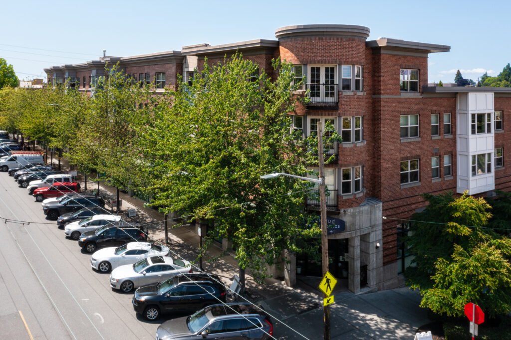 Modern brick apartment building exterior in Seattle with curved architectural features, white trim, large windows, street-level parking lot with trees, professional real estate photography